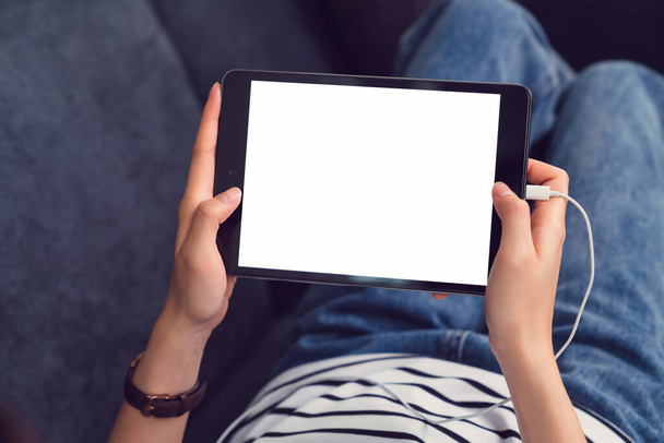 Femme tenant une maquette de tablette numérique de l'écran blanc et utilisant le mode de vie sur le canapé dans la maison. - Photo, image