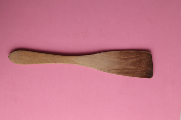 A closeup shot of a wooden cooking spoon on a pink background - Foto, Bild