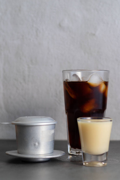 Вертикальний знімок склянки замороженої кави, сконденсованого молока та в'єтнамського кавового фільтра. - Фото, зображення