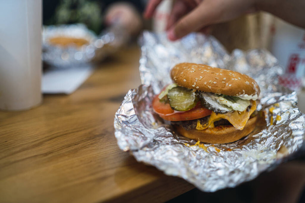 A selective focus shot of cheeseburger in a foil on a table - Foto, Bild