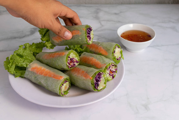 A closeup shot of a person picking a Vietnamese spring roll from a plate on a white table - Photo, image