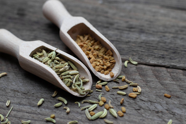 A closeup shot of fennel and fenugreek seeds in wooden spice spoons on a dark wooden surface - Foto, imagen