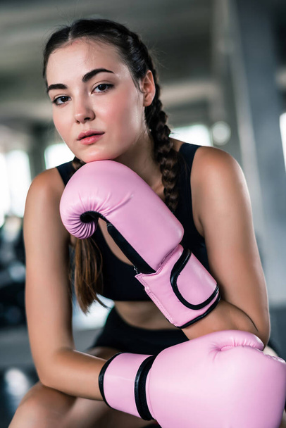 Attractive young Caucasian woman in boxing gloves. fashionable studio portrait of an sporty lady at gym background  - 写真・画像