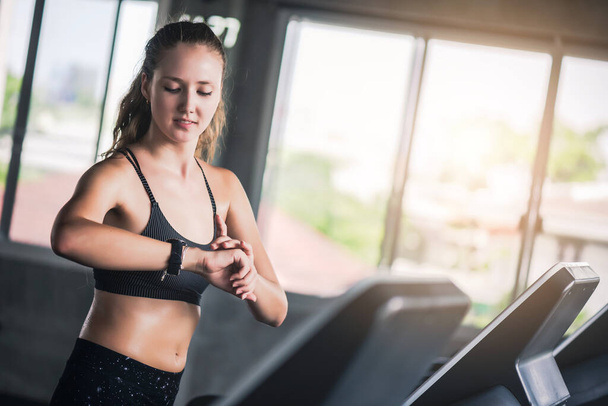 Attraktive hübsche Kaukasierin läuft auf Laufband und überprüft Herzfrequenz mit Smartwatch im Fitnessstudio.  - Foto, Bild