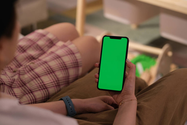緑の画面の携帯電話を持っている女性の肩越しに - 写真・画像