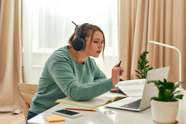 Interesting online course. Young beautiful woman, female student wearing headphones, looking at laptop screen while studying at home - Φωτογραφία, εικόνα