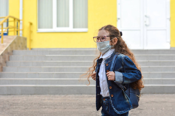 Back to school. Schoolgirl wearing medical face mask to health protection from influenza virus. Child going school after pandemic over.Portrait of a schoolgirl on the background of the school - Foto, Imagem