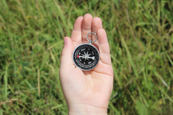 Old classic navigation compass in hand on natural background as symbol of tourism with compass, travel with compass and outdoor activities with compass - Photo, Image
