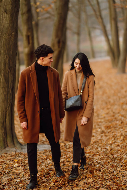 Young couple in love walking in the park on a autumn day. Enjoying time together. Stylish and loving couple enjoying each other in the autumn forest.  - Fotoğraf, Görsel