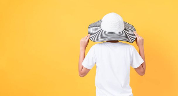 The woman stands behind and wears a wide-brimmed hat on an orange background. - Foto, Imagen