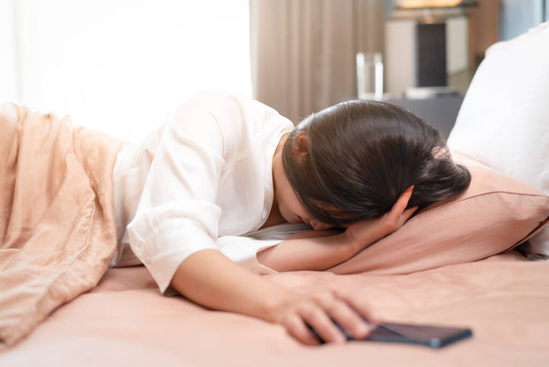 mujer somnolienta apagar la alarma en el teléfono inteligente mientras duerme en la cama - Foto, imagen