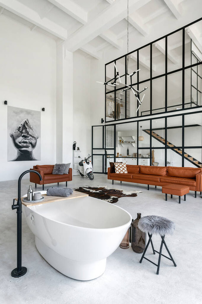 Pystysuora kuva huoneen moderni talo valoisa kylpyhuone ja viihtyisä olohuone, valkoinen mukava kylpy, sohva ja talon sisustus taustalla - Valokuva, kuva