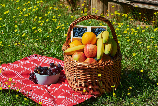 Basket of various fruits in the sunlight on a meadow with yellow flowers. - Photo, Image