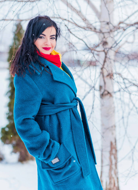 Koncepcja ferii zimowych. Arabska kobieta w stylowym spojrzeniu na śnieżny dzień na zewnątrz. Kobieta w niebieskim płaszczu alpaka i czerwono-żółty szalik w zimowy dzień na zewnątrz - Zdjęcie, obraz