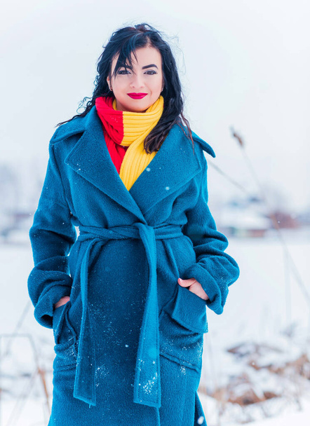 Concepto de vacaciones de invierno. Mujer árabe en la mirada elegante en el día nevado fuera. Mujer con abrigo azul alpaca y bufanda rojo-amarilla en el día de invierno al aire libre - Foto, Imagen