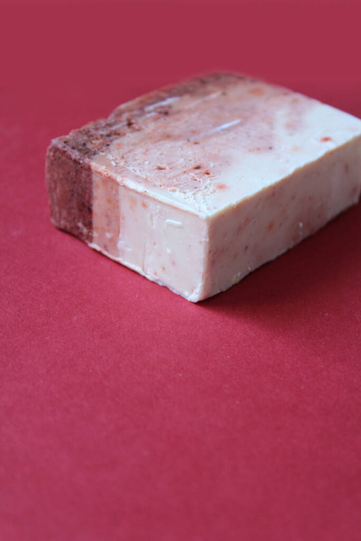 Un solo bloque de jabón hecho en casa sobre un fondo rojo oscuro. Jabón hecho a mano con el concepto de ingredientes naturales, vista de ángulo alto. Copyspace a continuación. - Foto, imagen