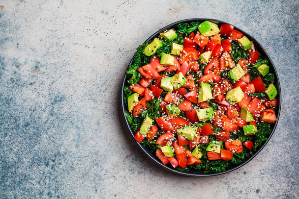 Kale salad with tomatoes and avocado in a black plate. Healthy raw vegan lunch concept. - Фото, зображення