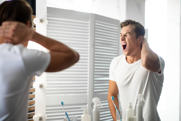 Handsome young man looking in the mirror and yawning - Photo, Image