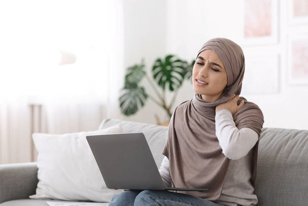 Ból szyi. Muzułmanka masuje podpaloną szyję zmęczoną pracą na laptopie - Zdjęcie, obraz