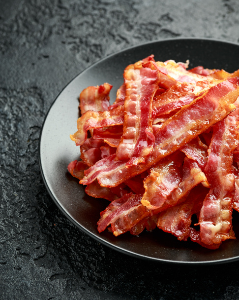 Fried crunchy Streaky Bacon pieces in a black plate - Photo, Image
