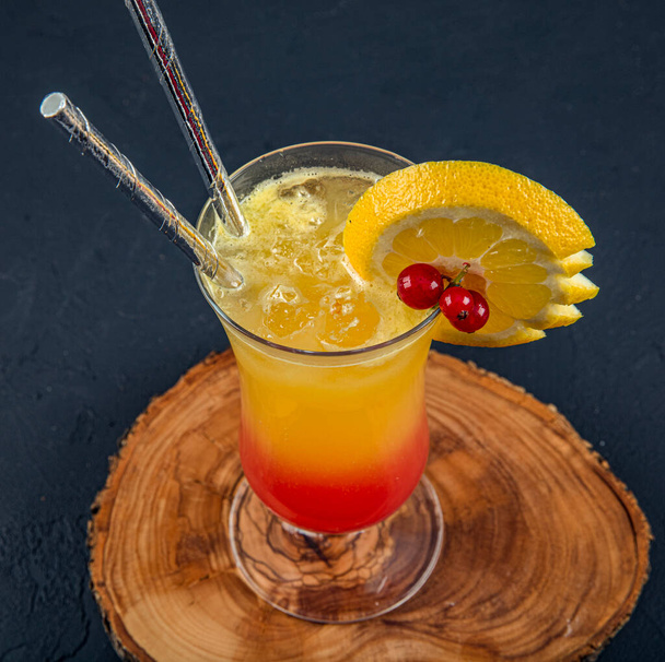 Juicy Orange and Red Tequila Sunrise with a Cherry. Tequila sunrise cocktail on dark wooden table. - Photo, Image