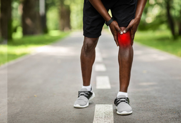 Oříznutý černý sportovec dotýkající se jeho zaníceného kolena - Fotografie, Obrázek