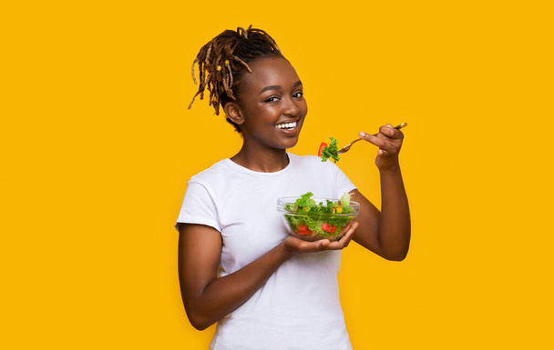 Gezonde Afrikaanse vrouw die verse salade eet boven geel - Foto, afbeelding