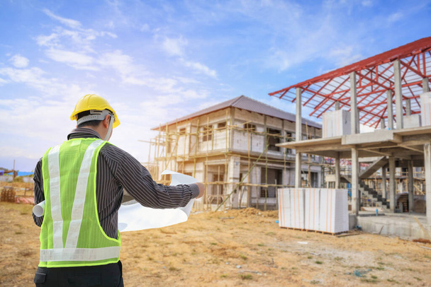Professionele ingenieur architect werknemer met beschermende helm en blauwdrukken papier op huis bouwplaats achtergrond - Foto, afbeelding