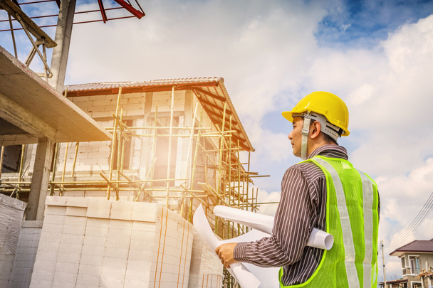 Asiático hombre de negocios ingeniero de construcción trabajador en casco de protección y planos de papel en la mano en la obra de la casa - Foto, imagen