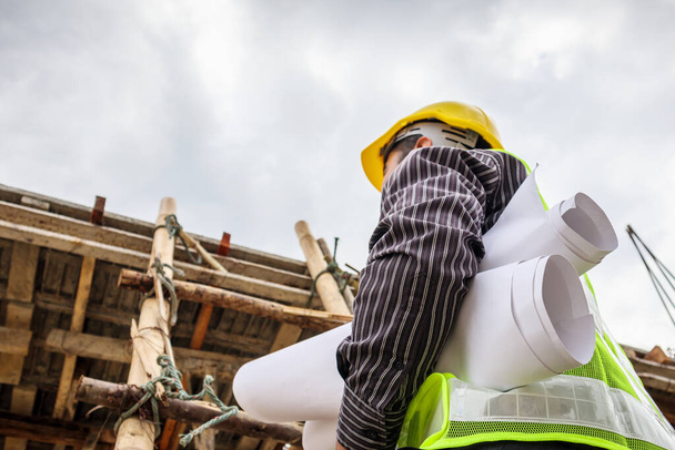 молодий професійний інженер-працівник в захисному шоломі і кресленнях паперу на руці, що працює на сходах на будівельному майданчику будинку
 - Фото, зображення