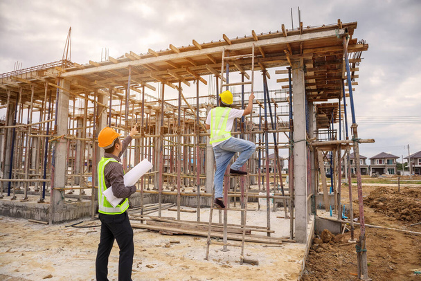 Aziatisch zakenman bouw manager en ingenieur werknemer in beschermende helm houden blauwdrukken papier bij de hand op de bouwplaats - Foto, afbeelding