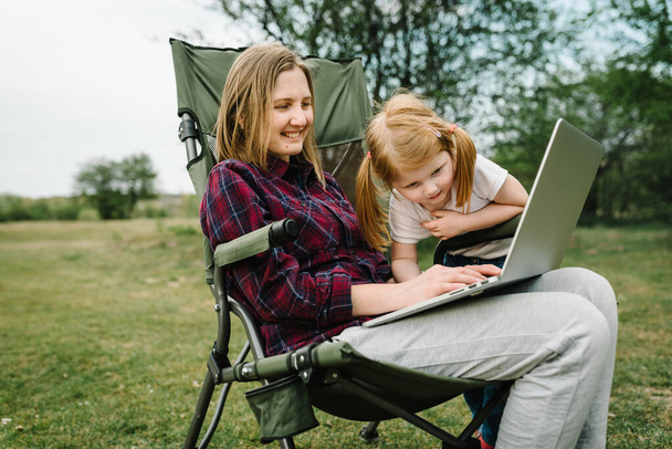 Chat online with family on laptop on picnic in nature. Homeschooling, freelance job. Mom and child. Mother work on Internet with kid outdoors. Quarantine, closed nursery school during coronavirus. - Фото, зображення