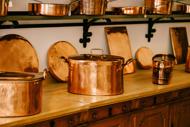 Grands pots en cuivre avec sous-verres chauds sur le comptoir avec casseroles en cuivre et casseroles sur des étagères à fixer au mur blanc. - Photo, image