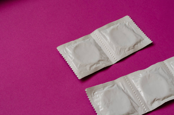 Vier Kondome auf lila Hintergrund verpackt. Fruchtbarkeitskontrolle. Schutz vor sexuell übertragbaren Krankheiten. - Foto, Bild