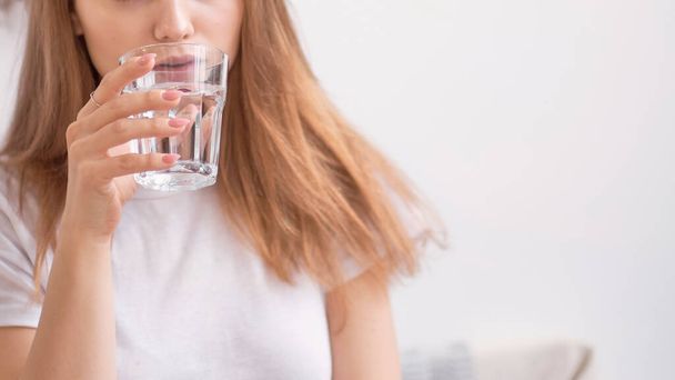 Красивая неузнаваемая молодая девушка пьет воду из стекла. Счастливая молодая женщина пьет воду. Улыбающаяся кавказская модель с прозрачным стеклом в руке. Крупный план. - Фото, изображение