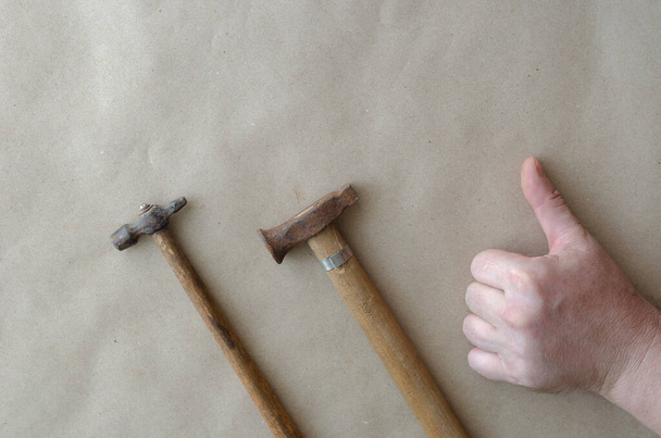 Caucasian man showing thumb up next to small hammers. The hand of a middle-aged man and two old hammers. Craftsman. Selective focus. - Photo, Image