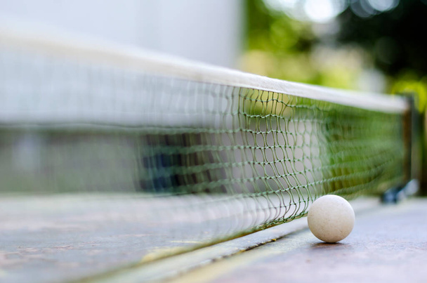 Zbliżenie piłki do ping ponga obok siatki na stole tenisowym. Metalowy stół do tenisa do uprawiania sportu na świeżym powietrzu. Aktywny tryb życia. Skupienie selektywne. - Zdjęcie, obraz