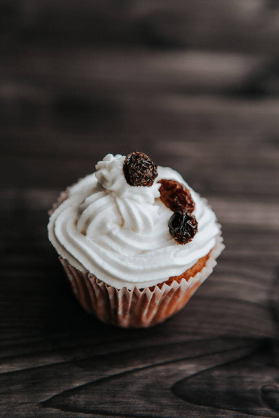 muffin with cream and raisins on a dark wooden background - Fotoğraf, Görsel