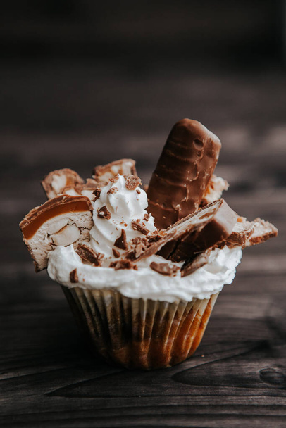 cupcake caseiro com creme branco e chocolate com nozes em um fundo escuro
 - Foto, Imagem