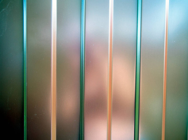 Cerca de perfil de metal verde e marrom com um padrão de linhas verticais ou tiras com uma estrutura escalonada e uma textura convexa ou fundo
. - Foto, Imagem