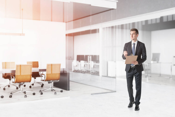 Confident young businessman with clipboard walking in modern office. Concept of management. Toned image - 写真・画像