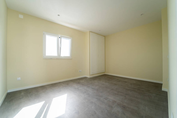 Empty room with dark wooden floating laminate flooring and wardrobe. House interior, wide bedroom space. Newly recently painted new apartment or house. Wood floor. Real state and property management - Photo, Image