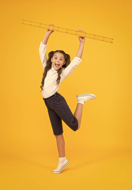 Exploring stem. Sizing and measuring. Pupil cute girl with big ruler. Geometry school subject. School adorable student study geometry. Kid school uniform hold ruler. Education and school concept - 写真・画像