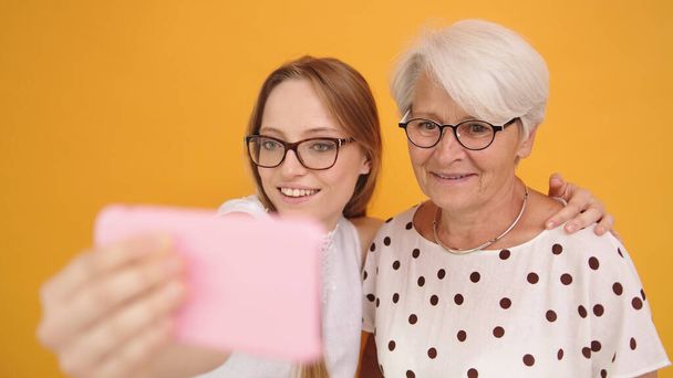 Senior and young woman taking selfies isolated on orange background - Foto, afbeelding