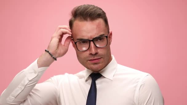 confused elegant businessman in white shirt wearing glasses, scratching head trying to solve difficult problems, pointing fingers up and having an idea, pointing finger to head and smiling on pink background - Footage, Video