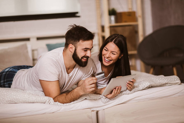 Молода пара купує онлайн від комфорту спальні та використовує цифровий планшет та кредитну картку
 - Фото, зображення