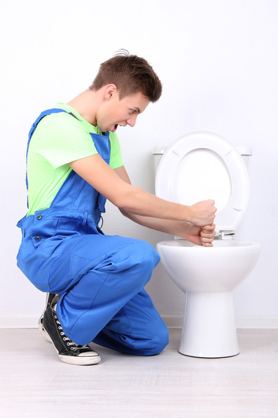 Plumber with toilet plunger on light background - Photo, Image
