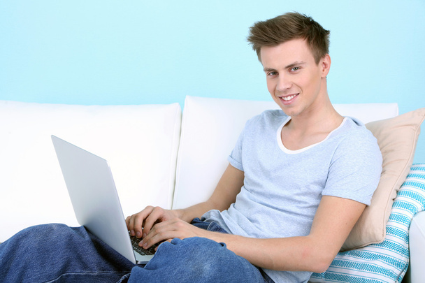 Guy sitting on sofa with laptop on blue background - Foto, imagen
