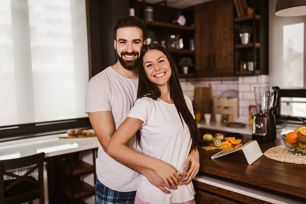 Joyful couple hugging in the kitchen at home in the morning - Фото, изображение