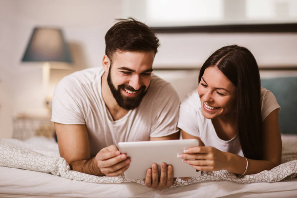 Hymyilevä rento nuori pari, joka käyttää digitaalista tablettia sängyssä kotona - Valokuva, kuva